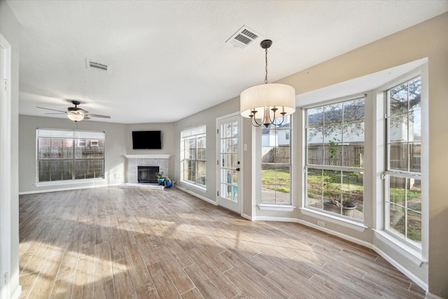 unfurnished living room with a glass covered fireplace, wood finished floors, visible vents, and baseboards