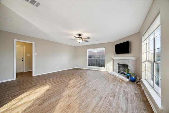 unfurnished living room with a ceiling fan, baseboards, wood finished floors, visible vents, and a fireplace