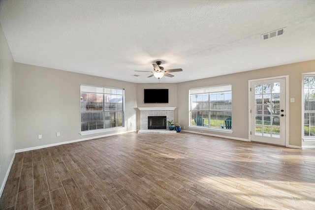 unfurnished living room with visible vents, a ceiling fan, wood finished floors, baseboards, and a brick fireplace