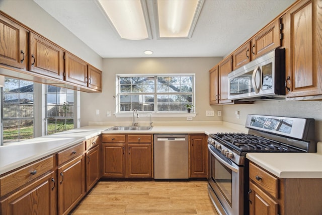 kitchen featuring light wood finished floors, light countertops, brown cabinets, appliances with stainless steel finishes, and a sink