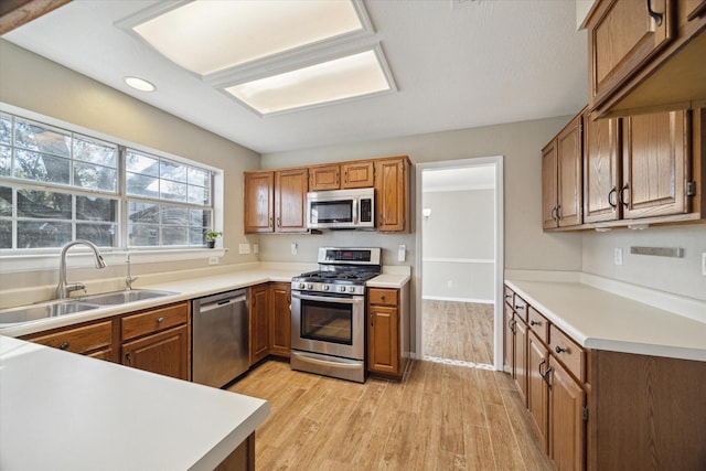 kitchen featuring a sink, light countertops, light wood-style floors, appliances with stainless steel finishes, and brown cabinets