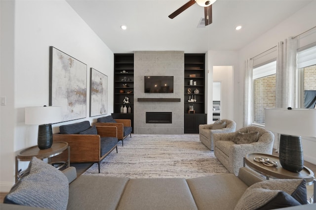 living room with a tiled fireplace, recessed lighting, built in shelves, and a ceiling fan