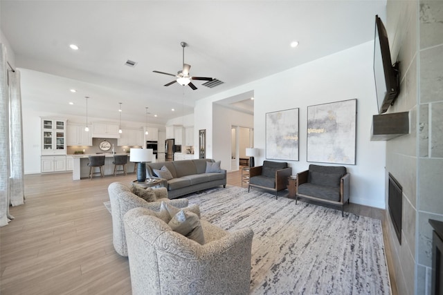 living room featuring visible vents, light wood-style flooring, a fireplace, and a ceiling fan