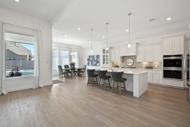 kitchen featuring tasteful backsplash, light wood finished floors, a center island with sink, light countertops, and a kitchen breakfast bar