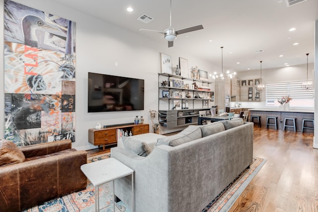 living area with light wood-style floors, recessed lighting, ceiling fan with notable chandelier, and visible vents