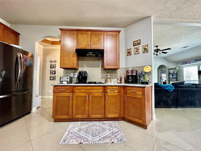 kitchen featuring arched walkways, black appliances, brown cabinetry, and under cabinet range hood