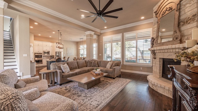 living room featuring crown molding, ceiling fan, dark wood finished floors, stairway, and a stone fireplace