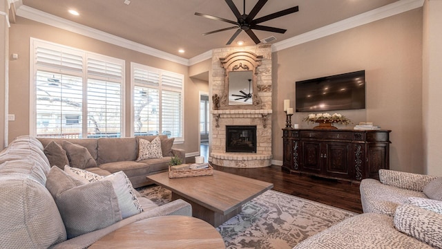 living room featuring dark wood-style floors, a ceiling fan, recessed lighting, a stone fireplace, and crown molding