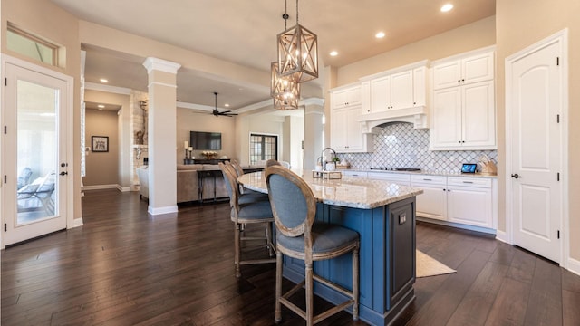 kitchen with light stone counters, backsplash, dark wood finished floors, white cabinets, and ornate columns