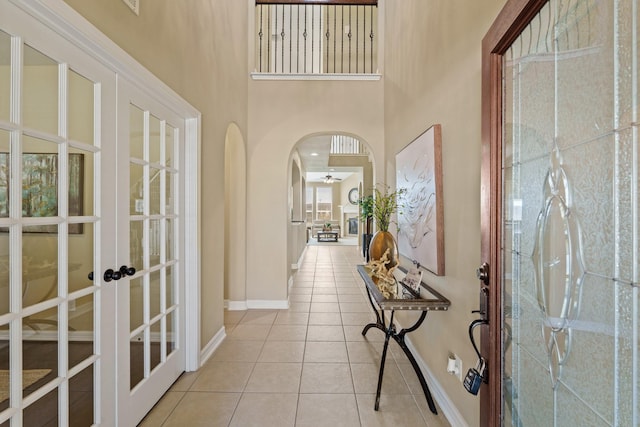 tiled entryway with french doors, baseboards, arched walkways, and a high ceiling