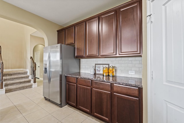 kitchen with dark stone countertops, stainless steel fridge, arched walkways, and light tile patterned flooring