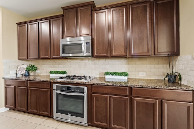 kitchen with decorative backsplash, dark stone counters, light tile patterned floors, and stainless steel appliances