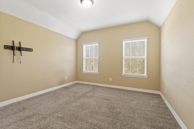 carpeted empty room featuring vaulted ceiling and baseboards