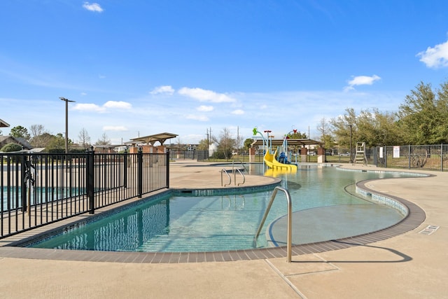 community pool with playground community, a patio, a water play area, and fence