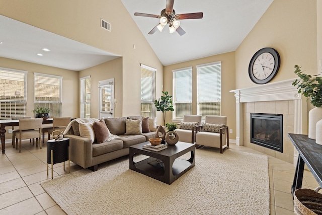 living room with visible vents, a tiled fireplace, light tile patterned floors, high vaulted ceiling, and a ceiling fan