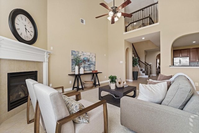 living room with stairway, baseboards, a fireplace, arched walkways, and ceiling fan