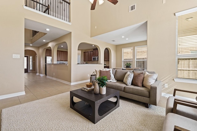 living room featuring light tile patterned floors, a ceiling fan, visible vents, arched walkways, and a towering ceiling