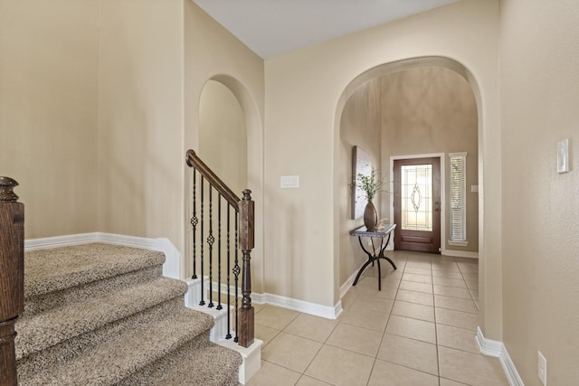 foyer with light tile patterned floors, baseboards, arched walkways, and stairs