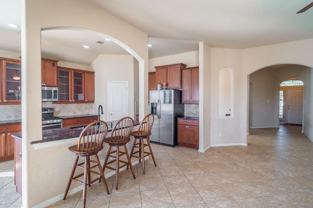 kitchen with decorative backsplash, brown cabinets, appliances with stainless steel finishes, arched walkways, and a sink