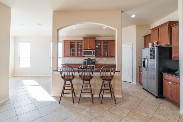 kitchen featuring backsplash, brown cabinets, stainless steel appliances, and a kitchen bar