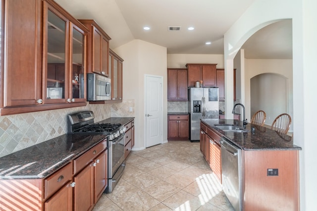 kitchen with vaulted ceiling, dark stone countertops, appliances with stainless steel finishes, arched walkways, and a sink