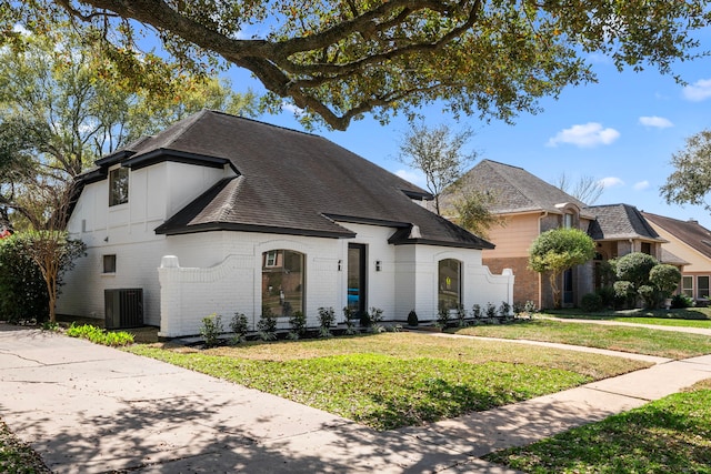 view of front of house featuring brick siding, cooling unit, a shingled roof, and a front yard