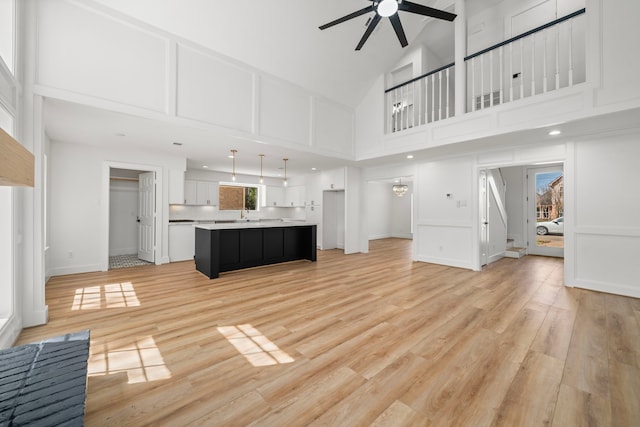 unfurnished living room with a decorative wall, a ceiling fan, light wood-type flooring, and high vaulted ceiling