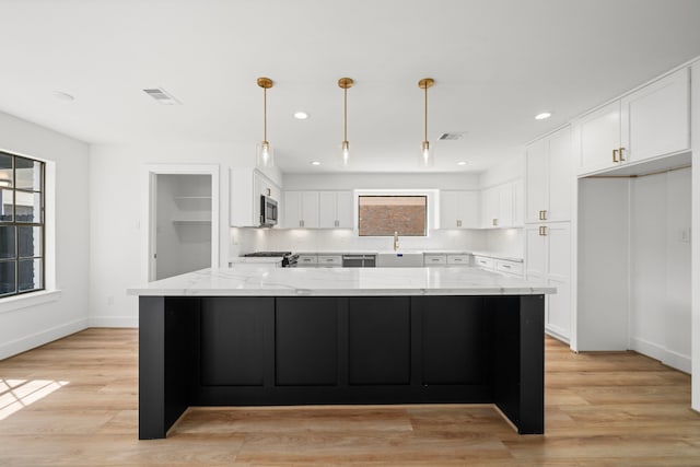 kitchen with visible vents, light stone counters, stainless steel microwave, white cabinets, and decorative backsplash