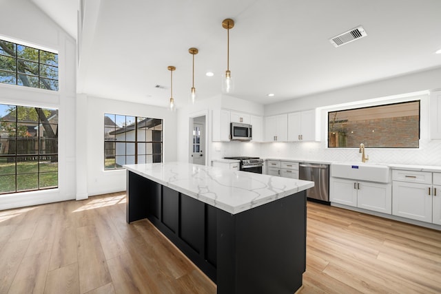 kitchen with a sink, backsplash, a kitchen island, appliances with stainless steel finishes, and light wood finished floors