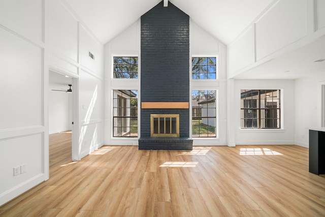 unfurnished living room featuring a ceiling fan, visible vents, light wood finished floors, high vaulted ceiling, and a brick fireplace