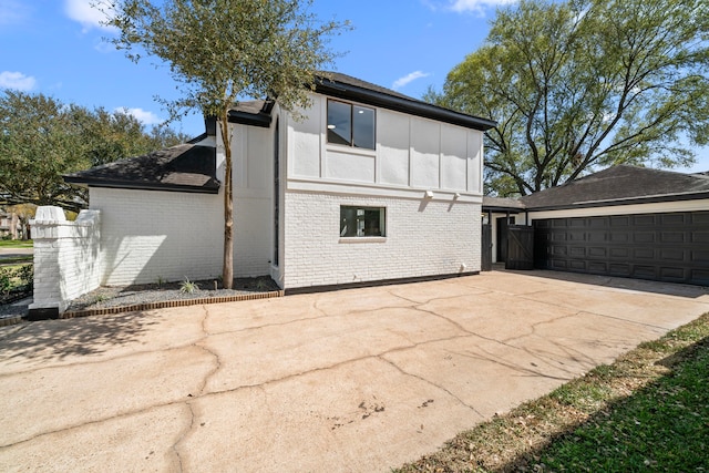 rear view of house with brick siding, board and batten siding, concrete driveway, and a garage