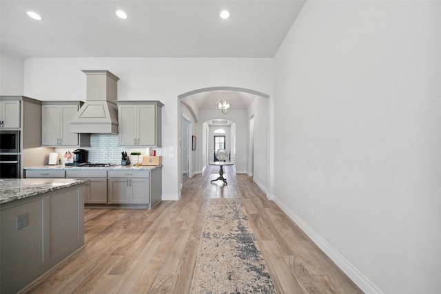 kitchen featuring gray cabinetry, light wood-style flooring, arched walkways, custom exhaust hood, and stainless steel appliances