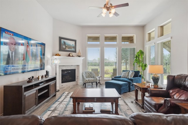 living room with a glass covered fireplace, a ceiling fan, light wood finished floors, and a healthy amount of sunlight