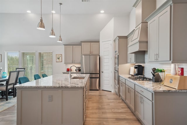 kitchen with an island with sink, gray cabinets, stainless steel appliances, custom range hood, and light wood-type flooring