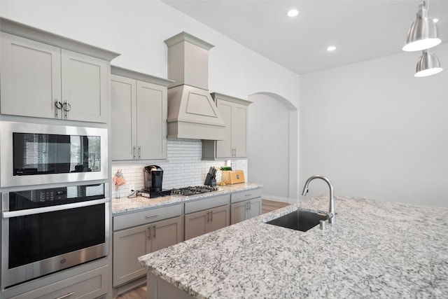 kitchen featuring tasteful backsplash, gray cabinetry, premium range hood, built in microwave, and a sink