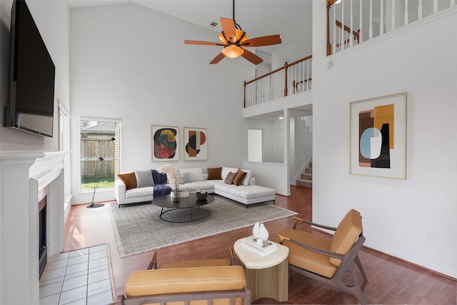 living room with wood finished floors, stairs, ceiling fan, high vaulted ceiling, and a fireplace with flush hearth