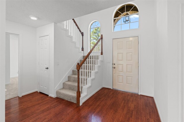 entrance foyer featuring dark wood finished floors, stairway, a textured ceiling, and baseboards