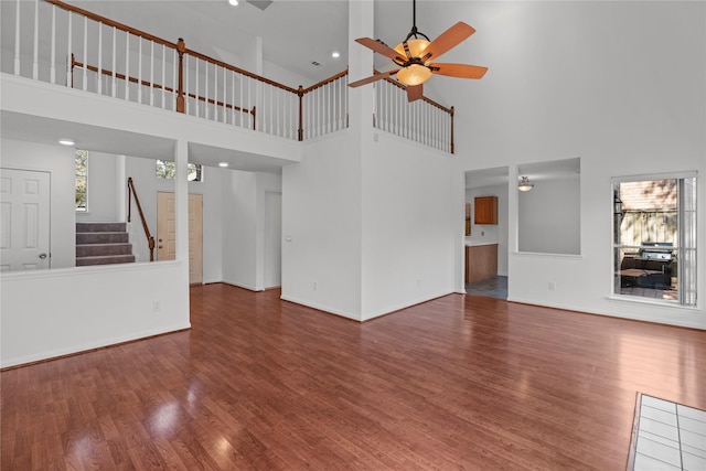 unfurnished living room featuring stairway, a ceiling fan, baseboards, a towering ceiling, and wood finished floors
