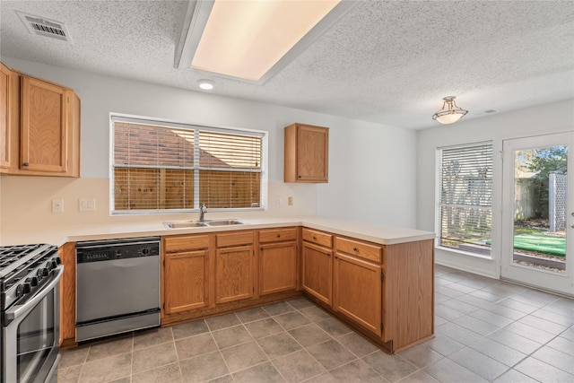 kitchen featuring a textured ceiling, a sink, appliances with stainless steel finishes, visible vents, and a peninsula