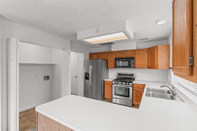 kitchen with a peninsula, a sink, appliances with stainless steel finishes, and visible vents