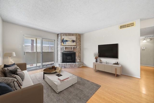 living room with visible vents, a textured ceiling, wood finished floors, and a fireplace