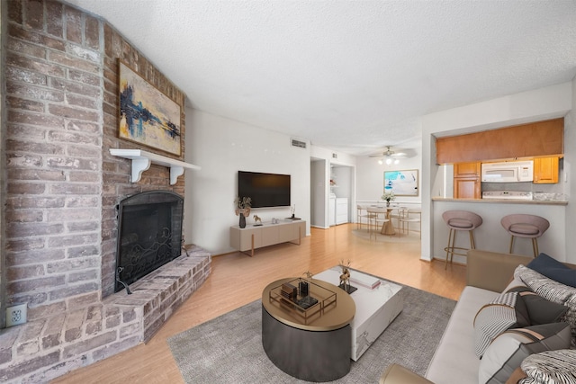 living area with visible vents, a brick fireplace, ceiling fan, and wood finished floors