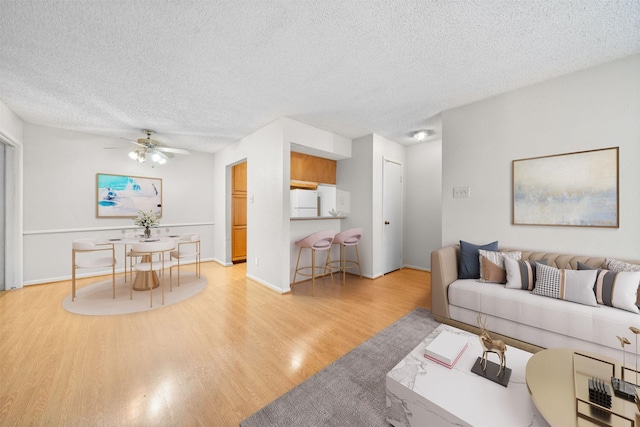 living area featuring baseboards, a textured ceiling, ceiling fan, and wood finished floors