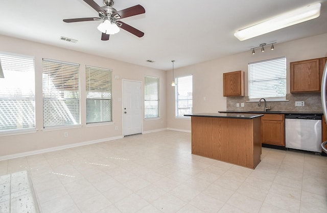 kitchen featuring a sink, a kitchen island, stainless steel dishwasher, dark countertops, and decorative backsplash