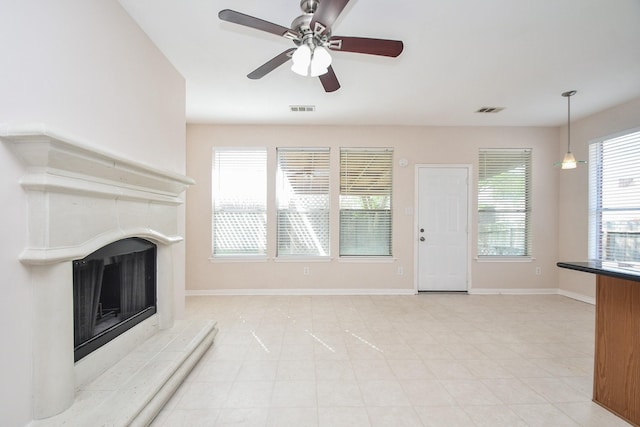 unfurnished living room featuring visible vents, a fireplace with raised hearth, baseboards, and ceiling fan