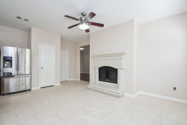 unfurnished living room featuring a fireplace with raised hearth, a ceiling fan, visible vents, and baseboards