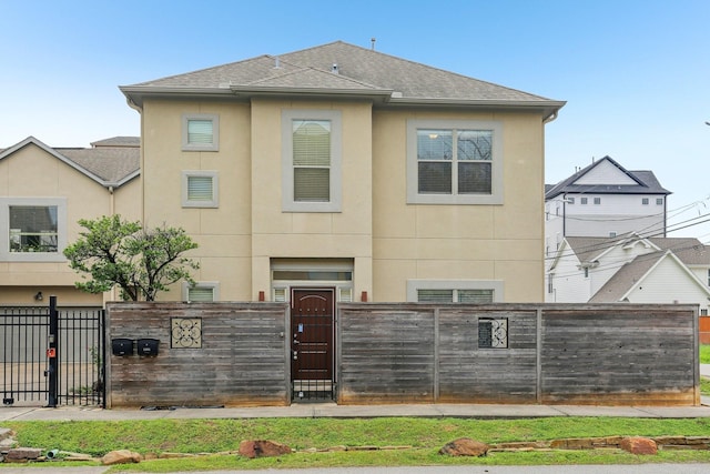 rear view of property featuring a fenced front yard, stucco siding, roof with shingles, and a gate