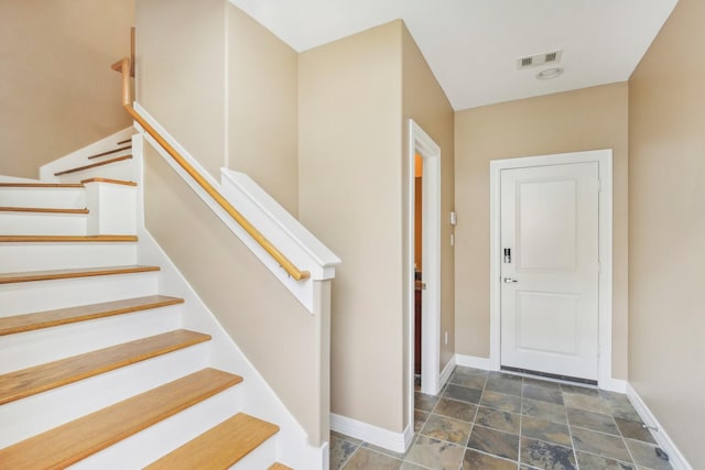 foyer featuring visible vents, baseboards, stone finish floor, and stairway