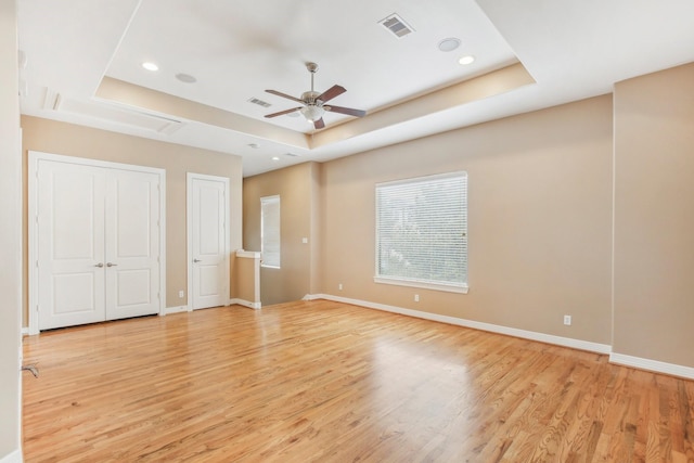 unfurnished bedroom with a raised ceiling, light wood-style flooring, and visible vents