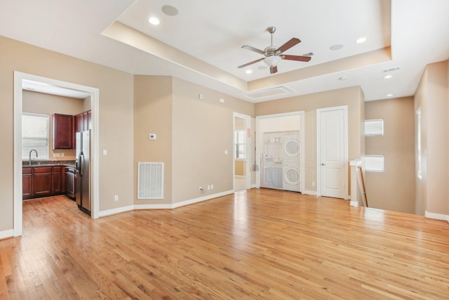 unfurnished living room with a ceiling fan, visible vents, light wood-style flooring, stacked washer and clothes dryer, and a raised ceiling